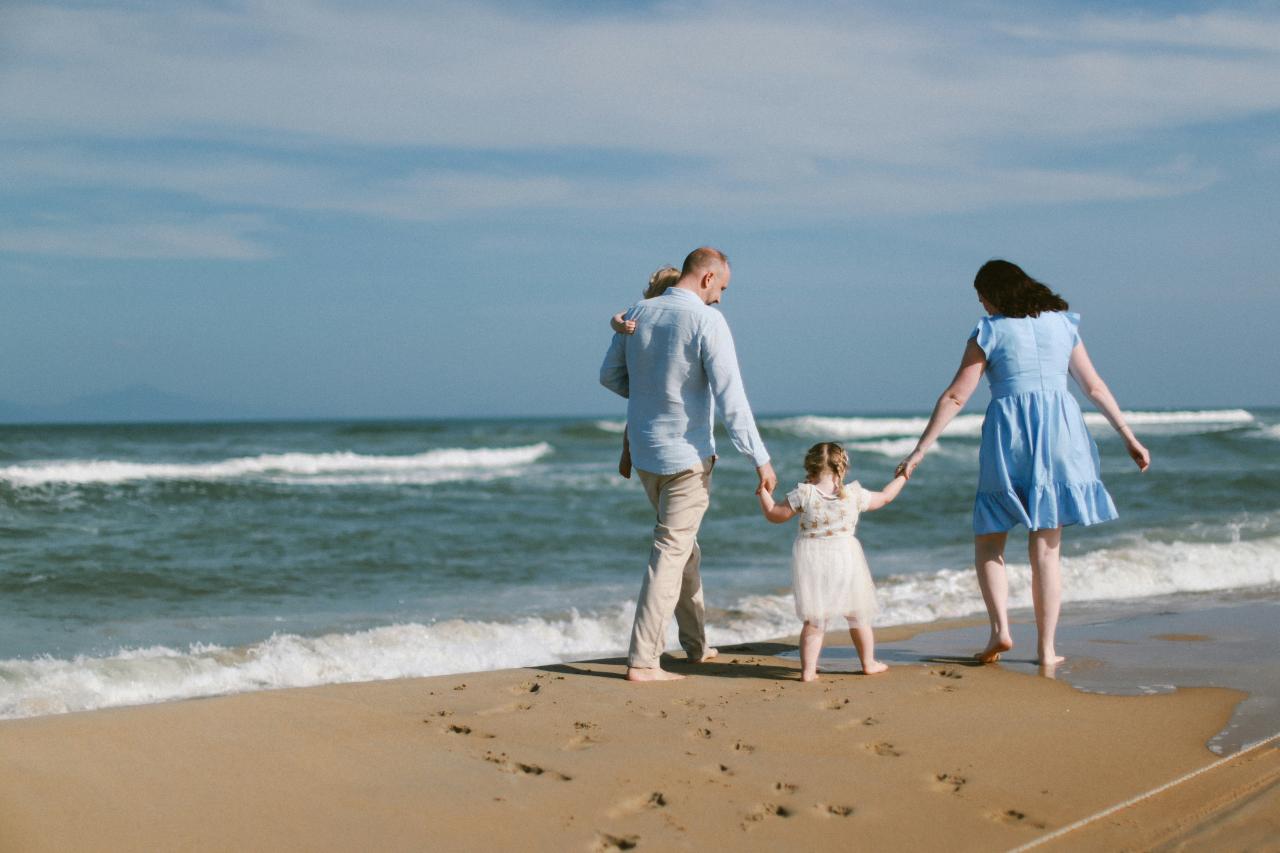 Family walks on the beach by the ocean.